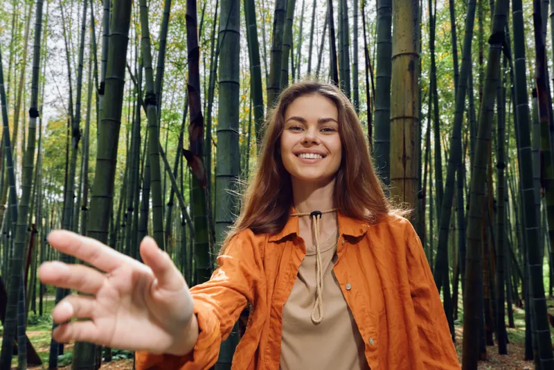 Woman smile bamboo forest reaching portrait nature outdoor young female person smiling and reaching hand toward camera in bamboo grove, candid joyful portrait with warm friendly expression