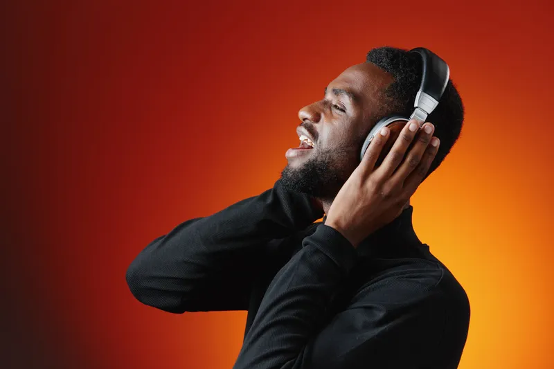 Young Black man enjoying music with headphones against a vibrant orange background, radiating joy and relaxation while listening to his favorite tunes