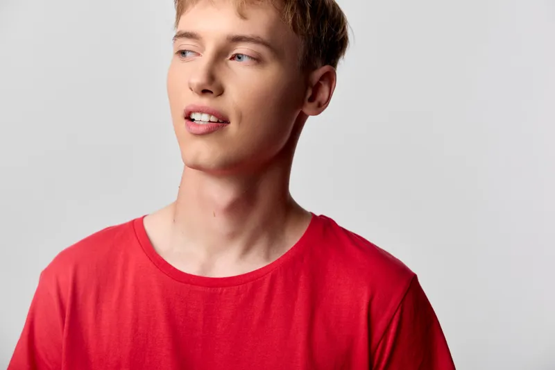 Young man wearing a bright redshirt, looking to the side with a relaxed smile, studio lighting and a clean background suitable for lifestyle, fashion or casual stock imagery