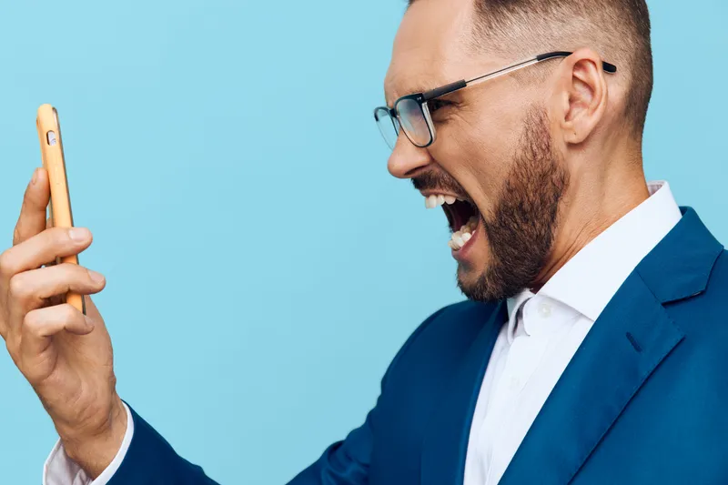A professional man in a blue suit on a colored isolated background radiates excitement and confidence while filming a quick video message on his phone.