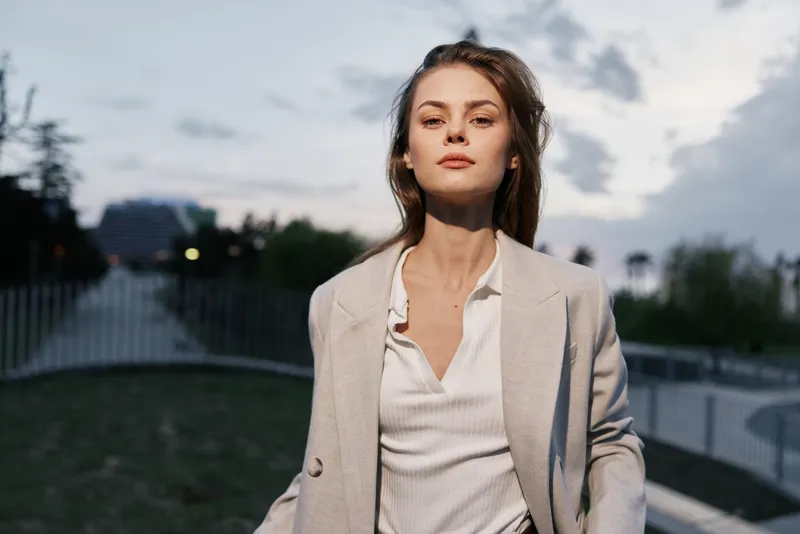 Businesswoman in a light blazer exuding confidence in an urban setting, capturing a modern professional vibe with a soft color palette at dusk.