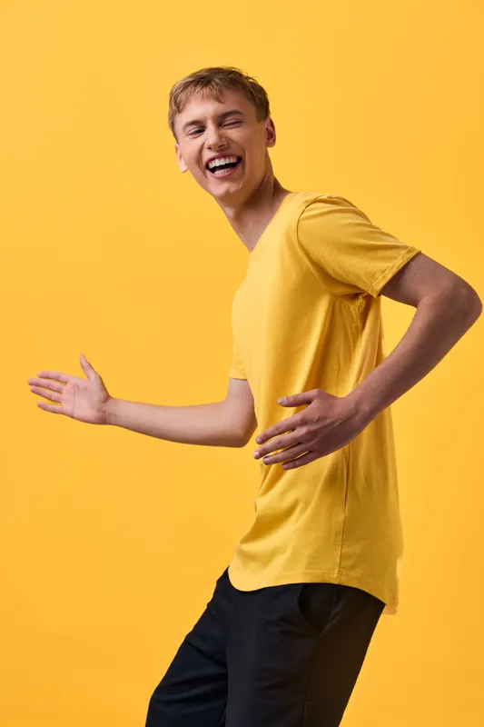 Joyful movement of a man in a yellow shirt, energetic and playful in a bright studio, expressing happiness and casual fashion in a dynamic frame.