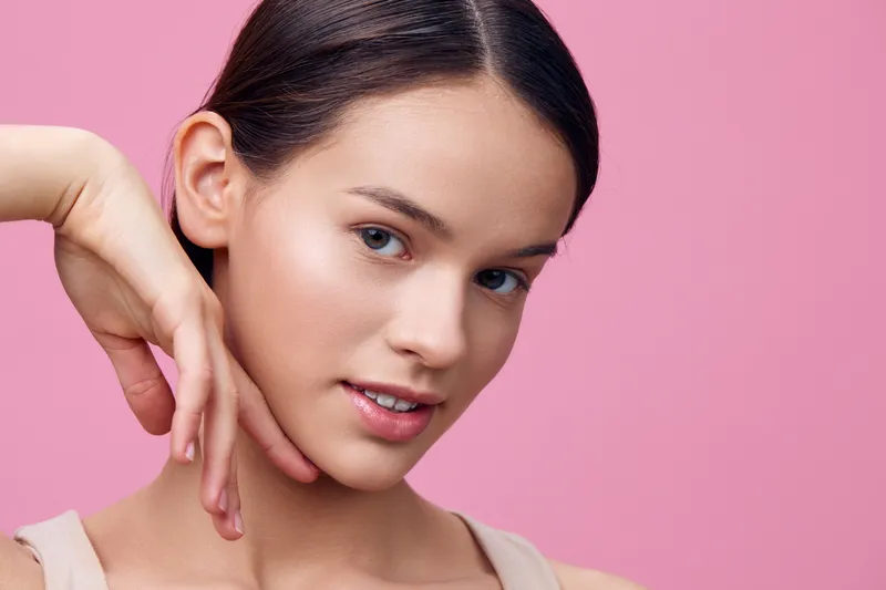 Portrait of a young model with a soft smile against a pastel pink background, showcasing natural beauty and elegance, perfect for beauty and skincare themes