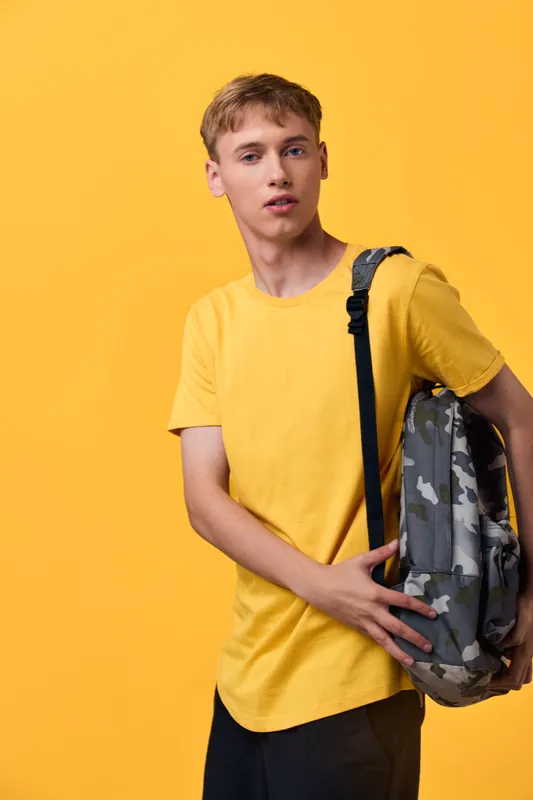 Backpack, youth, casual, student, fashion, travel, urban visuals of a young man with camo backpack against a bright yellow backdrop, signaling carefree style, school routine and daily commute in