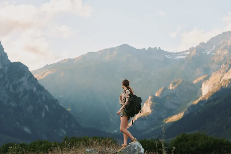 Woman hiker with backpack on a mountain trail, enjoying scenic views, outdoor lifestyle, sense of adventure, solitary moment in nature, framed by alpine scenery.