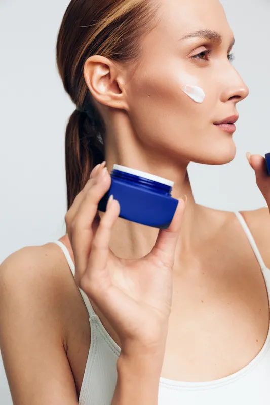 Woman skincare applying cream beauty routine, closeup profile on face, clean hygiene concept, spa care mood, soft natural light, neutral background, calm expression, healthy skin