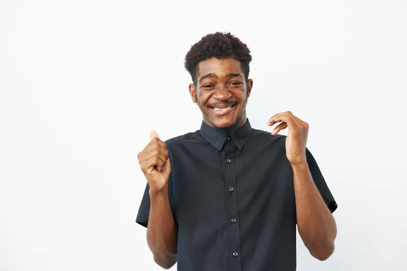Happy black man celebrating success with a joyful expression, dressed in a stylish black shirt, showcasing positive energy and confidence.
