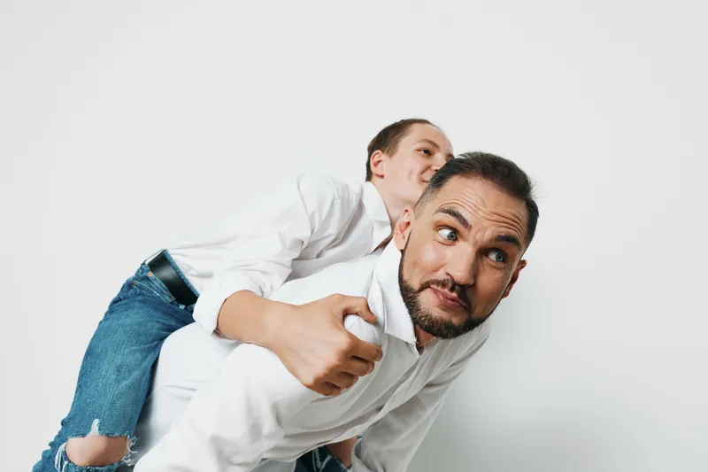 A professional man in business attire with a confident, upbeat mood, carrying a colleague on his back against an isolated colored background, portraying energy, teamwork, and a dynamic leadership