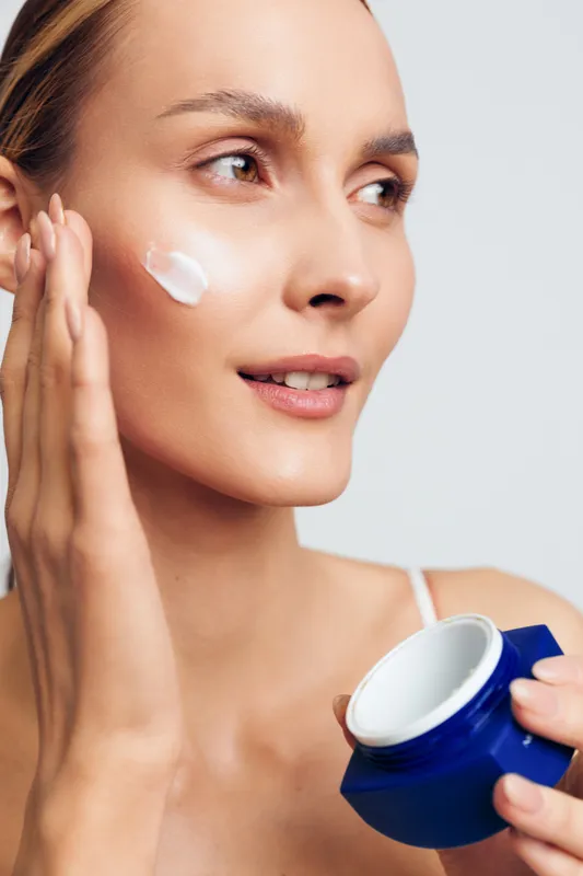 Woman skincare, face cream, moisturize cheek, beauty routine, hygiene care, indoor soft light, holding blue jar, smooth glow skin
