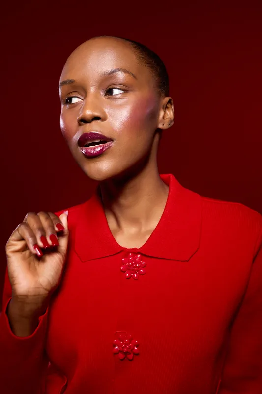 Portrait of elegant African woman with dark skin wearing red sweater with decorative buttons. She looks away in studio lighting. Concept of fashion, beauty, and confident female model.