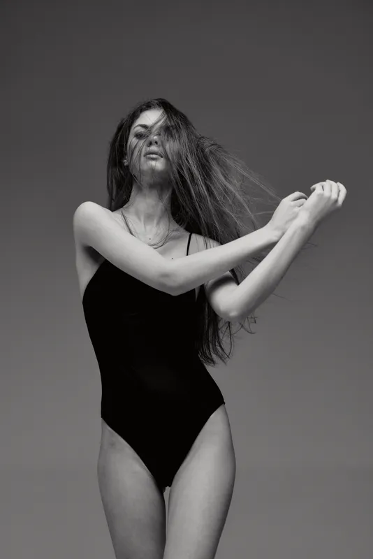 black and white woman posing in black swimsuit with flowing hair isolated on gray background