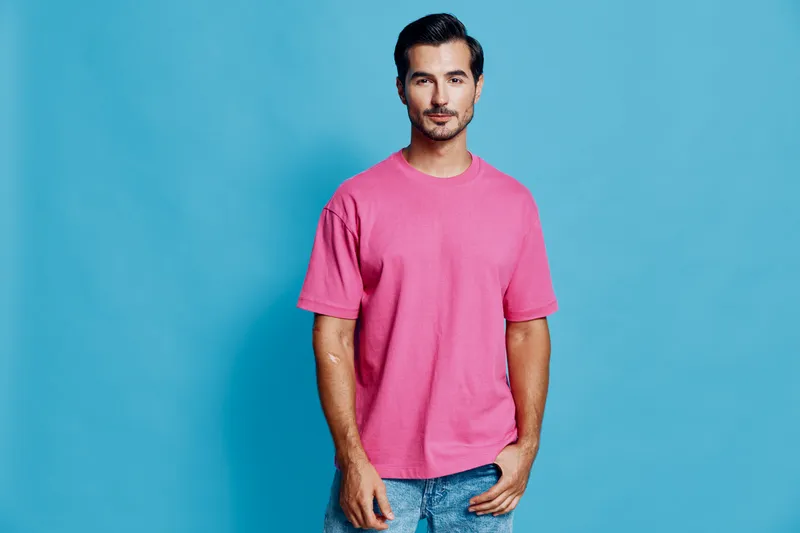 Handsome young man wearing a pink t-shirt stands confidently against a solid blue background, exuding a relaxed and approachable vibe. Portrait lifestyle concept.