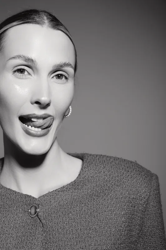 Portrait of a smiling white woman with light skin, showing playful expression with tongue out in black and white studio photo.