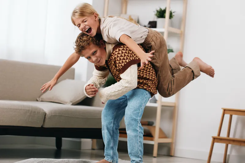 Authentic moment of playful bonding at home, featuring a child riding on a parent’s back, capturing genuine joy, movement, and everyday lifestyle in a cozy living room.