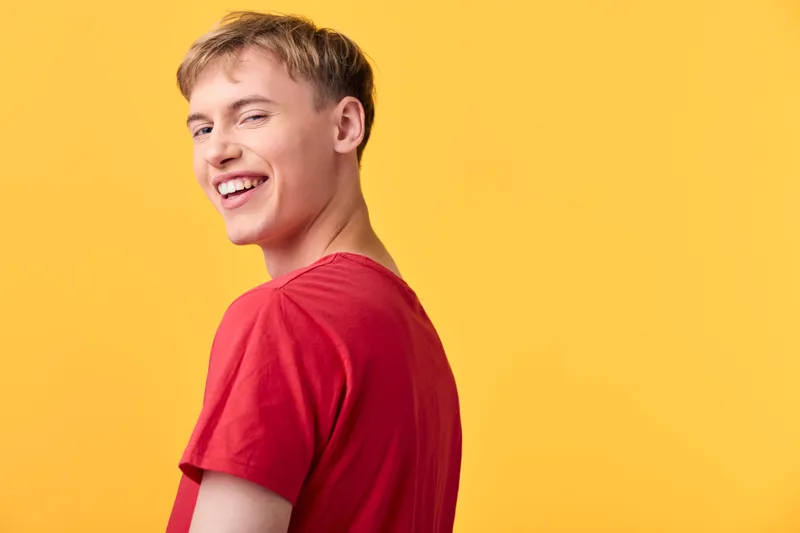 Smiling man in a red t shirt stands against a vibrant yellow backdrop, conveying youthfulness, confidence and positive energy for lifestyle, fashion and marketing visuals.