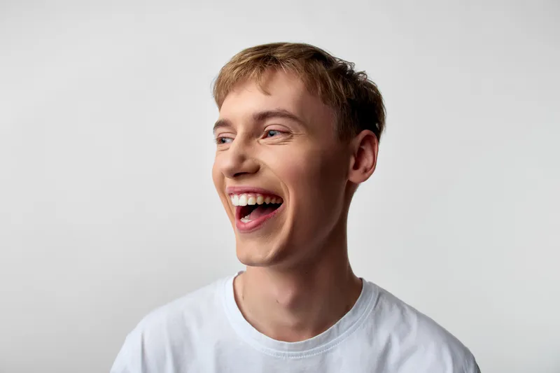 Laughter, happiness, smiling man in a casual white tshirt captures joy and energy in a candid studio moment, with a clean background, warm expression, and approachable vibe perfect for lifestyle and
