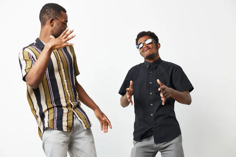 Two smiling African American men enjoying a fun moment together, dressed in stylish shirts and showcasing a vibrant atmosphere of friendship and celebration.