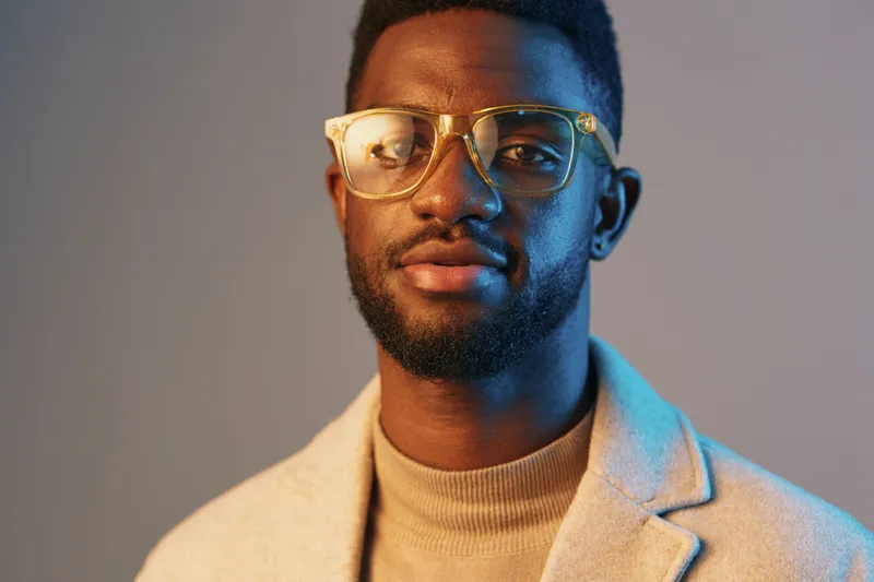Stylish young Black man in glasses and cozy sweater, exuding confidence in a blue and beige color palette, perfect for lifestyle and fashion concepts