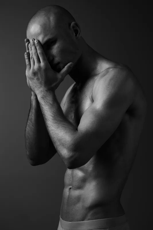 Black and white portrait of a man showing emotions, capturing vulnerability and strength in a dramatic pose with artistic lighting and shadow play.