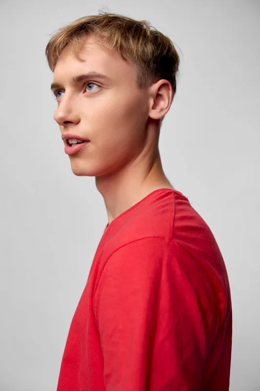 Young man in a red shirt, side profile against a plain backdrop, conveying focus and thoughtful mood, casual fashion and studio lighting for editorial use and clean visual storytelling