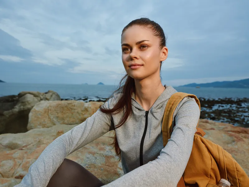 Young woman in a gray hoodie enjoying a serene coastal landscape, embodying tranquility and adventure, ideal for themes of healthy lifestyle and nature exploration