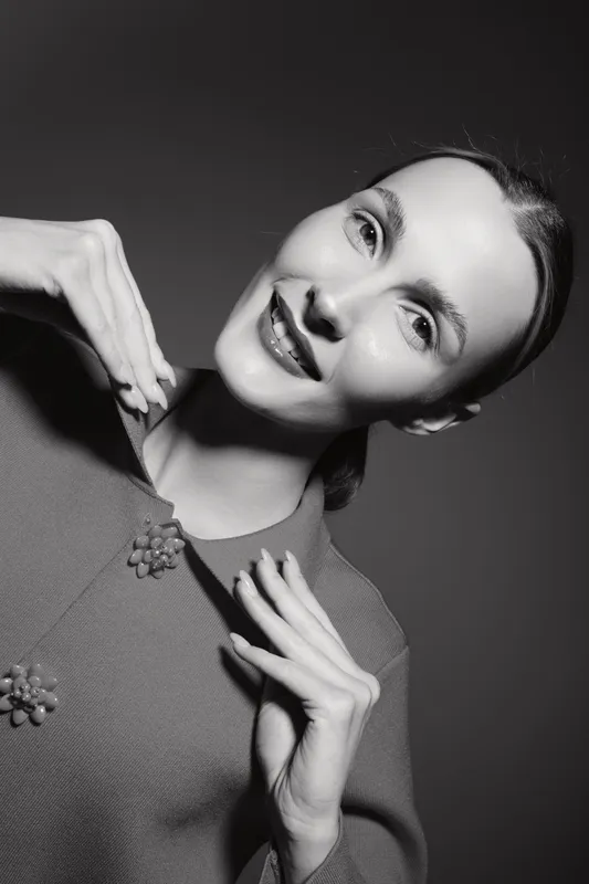 Portrait of a smiling Caucasian woman with light skin and dark hair posing in studio wearing a sweater with decorative buttons.