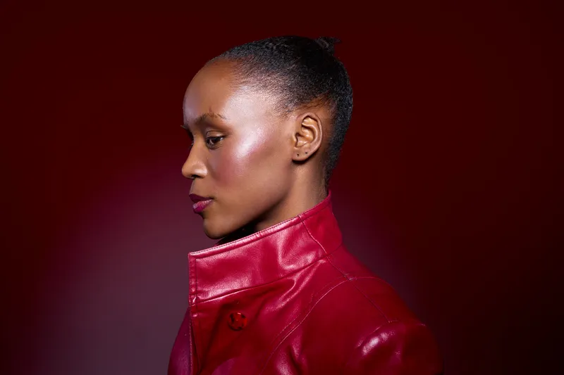 Profile of a confident dark skinned African woman in a red leather jacket against a red background. Concept for fashion, beauty, empowerment, and modern style portrait.