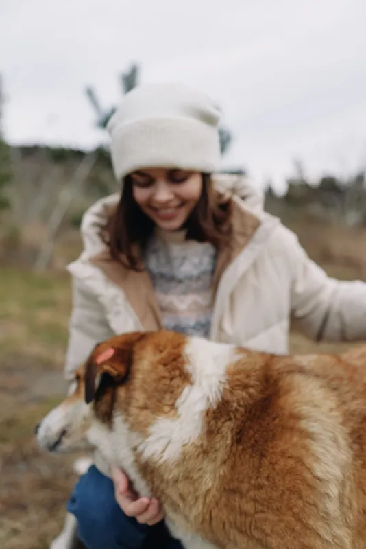 Woman and dog outdoors in park, capturing companionship with nature and affection, wearing a coat and winter outfit, joyful moment of bond and warmth under blueskies