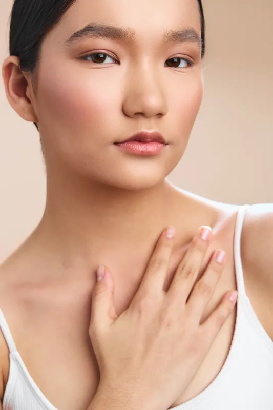 Asian woman with smooth skin appears in a close up portrait, showcasing a serene expression and graceful presence in a soft, neutral setting.