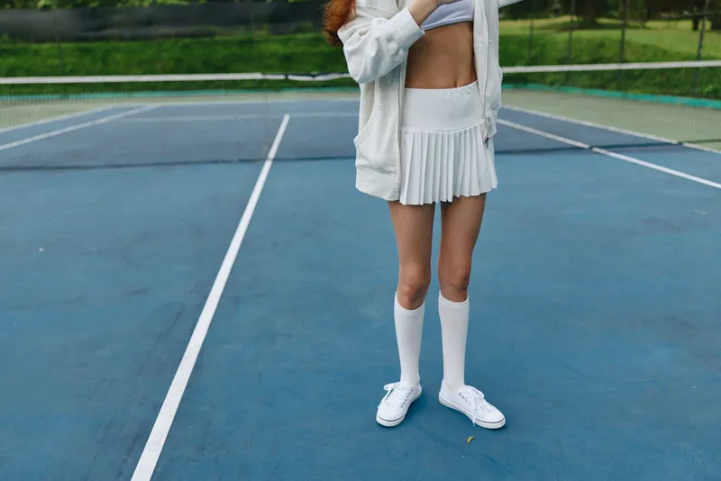Young female tennis player in white sportswear poses on a blue tennis court, showcasing athleticism and confidence, surrounded by a vibrant green background