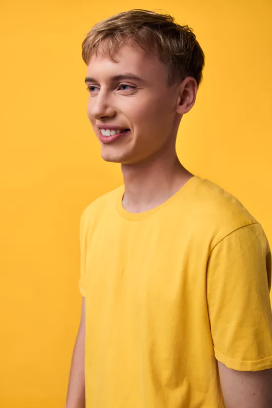 Smiling young man in a yellow tee against a vivid yellow backdrop, casual fashion, bright mood, friendly expression, light and color harmony, candid studio shot, everyday style