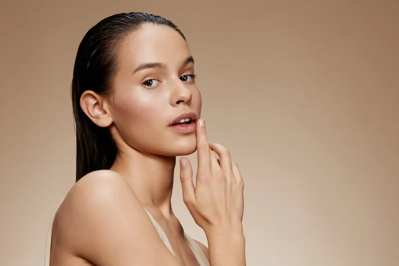 Portrait of a young woman with wet hair, natural makeup, and a subtle expression against a light, neutral background, ideal for beauty and skincare concepts