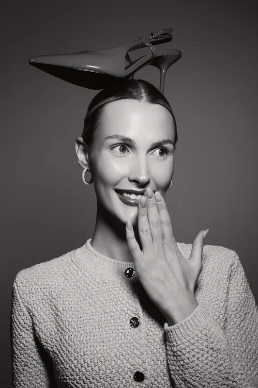 Happy caucasian woman with light skin wearing a high heel shoe on her head smiling and covering mouth in black and white image.