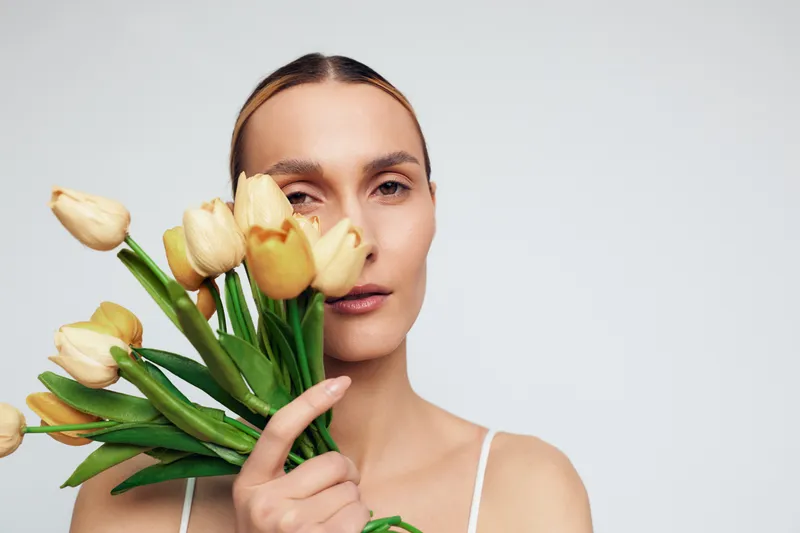 Young woman holds bouquet of yellow tulips close to her face with calm expression isolated on white background minimalistic floral concept.