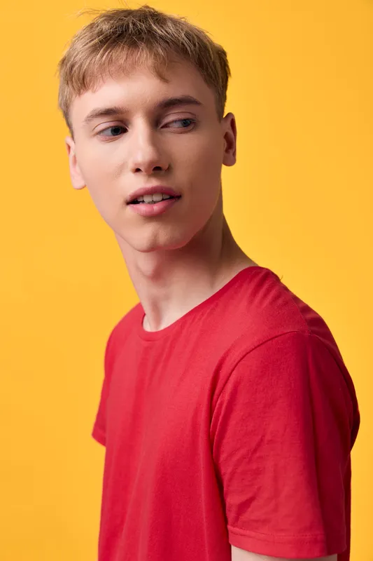Young man in a red t shirt against a bright yellow backdrop, thoughtful expression and casual stance, studio shot emphasizing fashion and lifestyle, clean studio lighting and color block