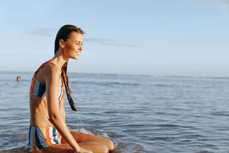 Woman on beach, ocean, sitting, bikini, sunlight, calm, relaxation, summer, seaside, wet sand, gentle waves, morning breeze, natural colors, serene face