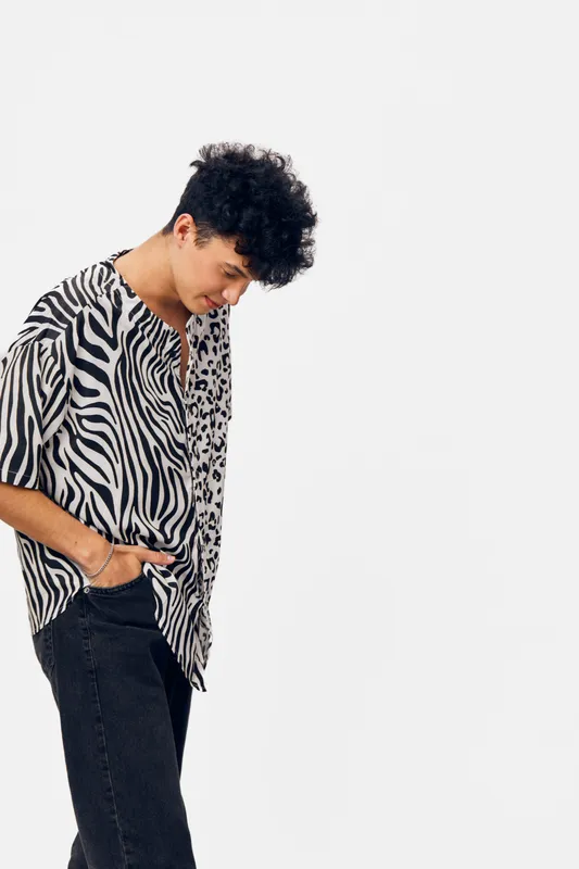 Young man in zebra print shirt looking down thoughtfully against a clean white background with casual style and relaxed posture.