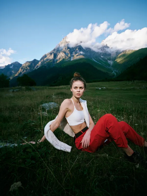 Woman seated on grass in a mountain meadow, outdoor nature scene with clear sky, casual athletic wear, and a calm, alpine countryside vibe for a lifestyle shoot
