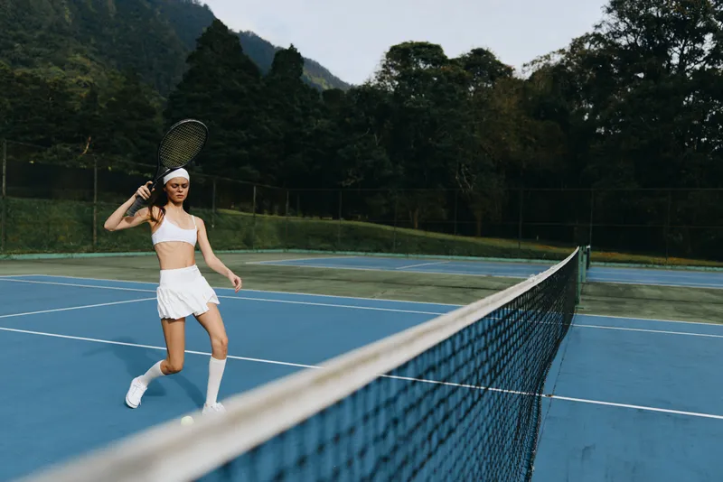 Young athletic woman playing tennis on outdoor court wearing white sportswear, showcasing determination while enjoying a sunny day in nature