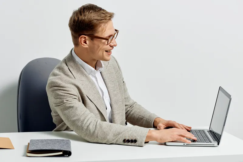 smiling man working on laptop in casual sweater using computer for remote freelance job with digital nomad concept isolated on white background studio