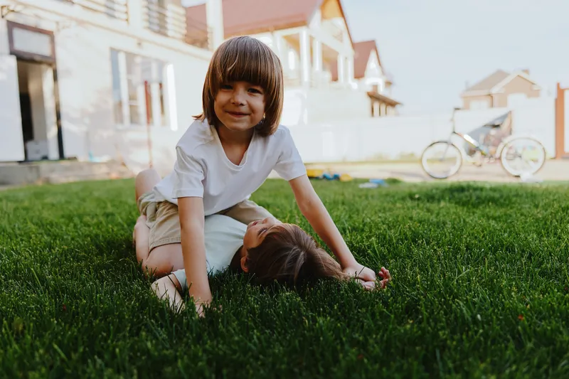 Happy children playing together on green grass in a sunny backyard, enjoying a carefree moment filled with laughter and joy, perfect for family themes.