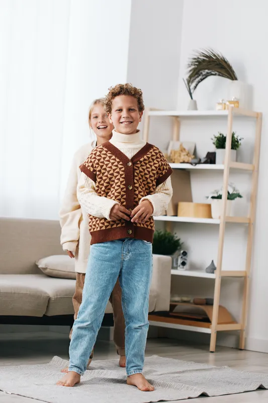 Authentic lifestyle scene featuring a cheerful pair at home, playful mood, warm knitwear, and simple school vibes, capturing everyday family moments and genuine connection.