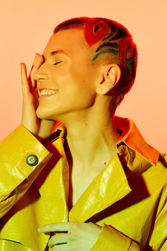 smiling woman with creative red hair tattoo and yellow jacket, posing joyfully against warm orange background, vibrant color contrast and modern style