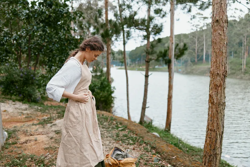 Young woman in a rustic dress standing by a serene river, showcasing nature s tranquility and a connection to the outdoors
