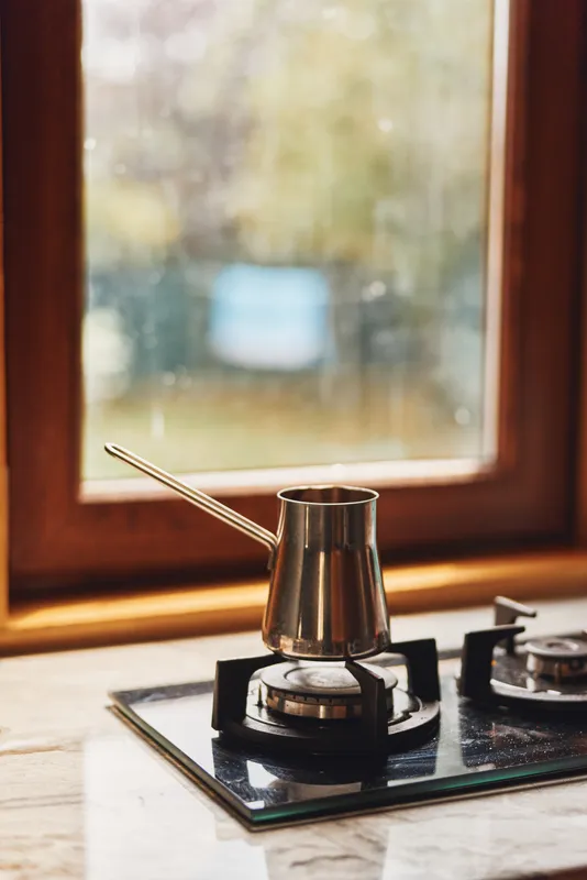 cezve coffee stove kitchen window morning pot gas steam metal cozy home countertop breakfast drink warmth vintage, cezve warming on gas burner by window with soft morning light and rustic kitchen mood