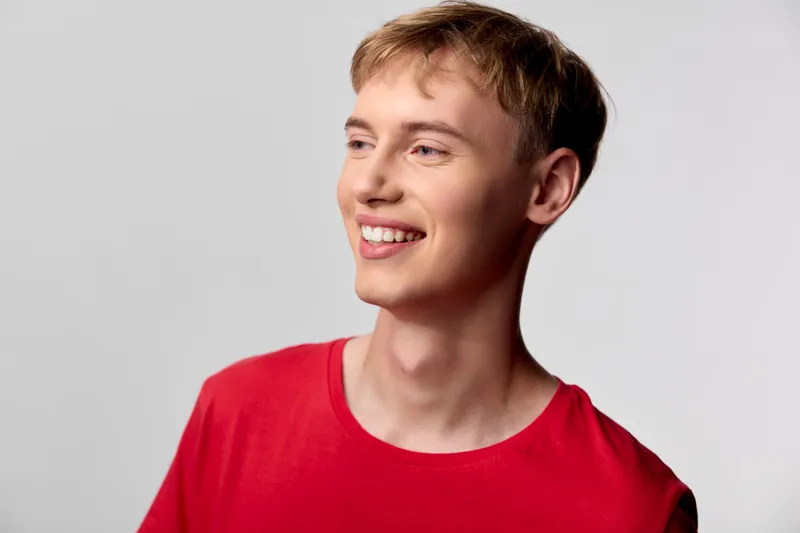 Smiling young man in a red shirt looking off to the side, casual mood, warm lighting, friendly and approachable expression, clean studio setting
