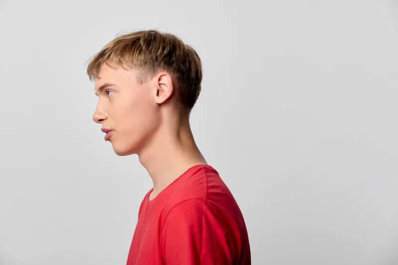 Profile of a man in a red shirt, side view in a studio with a neutral background, showcasing calm, thoughtful mood and minimalist composition for versatile use