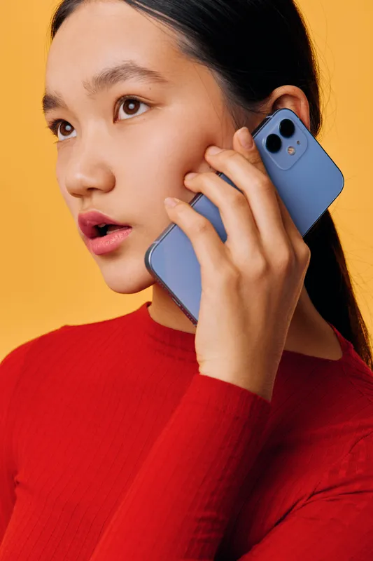Woman with long dark hair wearing red sweater holding smartphone to ear for phone call communication, closeup portrait with neutral orange background, technology and connection concept.