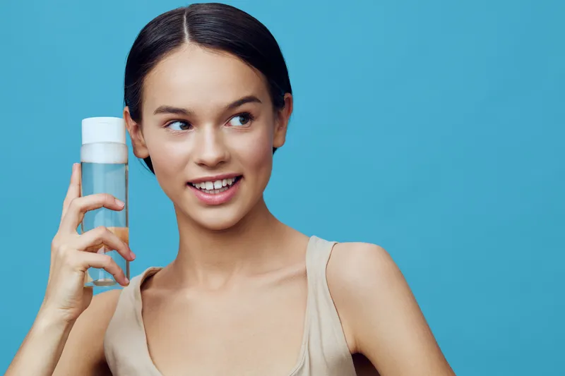 Confident young woman holding a water bottle against a vibrant blue background, showcasing healthy hydration and wellness concept