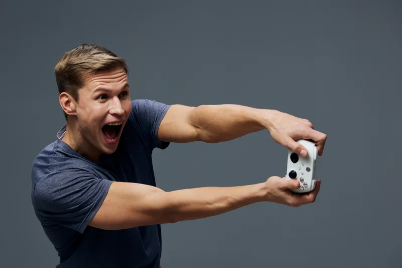 Joyful man taking selfie with smartphone, expressing excitement and happiness, casual blue t-shirt, gray background, close-up shot, lifestyle concept, modern technology, leisure activity.